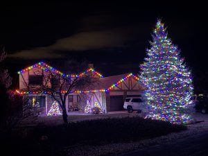 IMG_5181 | Reno Tahoe Holiday Lights Nighttime view of a house decorated with multicolored Christmas lights along the roofline and a large illuminated Christmas tree in the yard on the right.